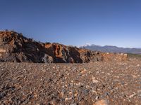 a dirt road next to the mountains with many rocks on it and a bench in front