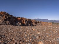 a dirt road next to the mountains with many rocks on it and a bench in front