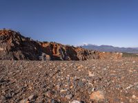 a dirt road next to the mountains with many rocks on it and a bench in front