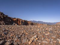 a dirt road next to the mountains with many rocks on it and a bench in front