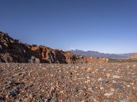 a dirt road next to the mountains with many rocks on it and a bench in front