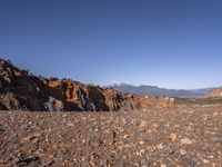 a dirt road next to the mountains with many rocks on it and a bench in front