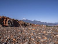 a dirt road next to the mountains with many rocks on it and a bench in front