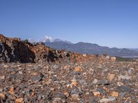 a dirt road next to the mountains with many rocks on it and a bench in front