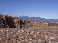 a dirt road next to the mountains with many rocks on it and a bench in front