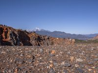 a dirt road next to the mountains with many rocks on it and a bench in front