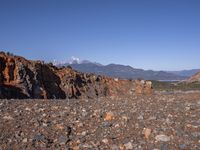 a dirt road next to the mountains with many rocks on it and a bench in front