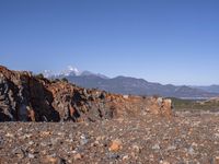 a dirt road next to the mountains with many rocks on it and a bench in front