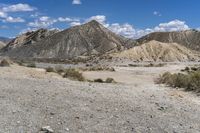 a dirt road leading through the desert with mountains behind it, and rocks on either side