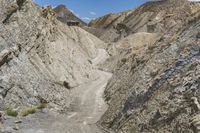 the dirt road runs along the rock sides near the mountain tops near the bottom of a dry canyon