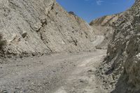 the dirt road runs along the rock sides near the mountain tops near the bottom of a dry canyon