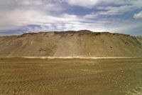 mountains with sand and dirt in front of it, and a car driving away in the distance