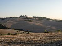 dirt road leading away from the camera, in a field near a farm area with hills