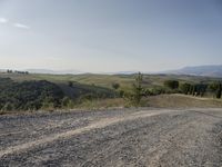 a small gravel road runs around an area with rolling hills and trees in the distance