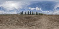 a panoramic view of a small dirt road in front of the sky and a bunch of trees on a hill