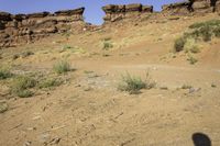 a dirt road in front of rocky cliffs in a desert area with plants and weeds