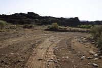 a dirt road with rocks on the sides in a rocky field of scrub and brush