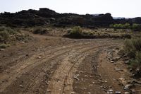 a dirt road with rocks on the sides in a rocky field of scrub and brush