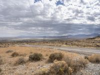 a dirt road leads down to an empty highway in the middle of nowhere with the mountains in the distance