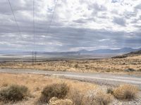 a dirt road leads down to an empty highway in the middle of nowhere with the mountains in the distance