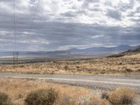 a dirt road leads down to an empty highway in the middle of nowhere with the mountains in the distance