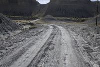 an empty dirt road passes across the desert plain, with large buttes in the background