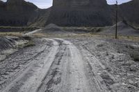 an empty dirt road passes across the desert plain, with large buttes in the background