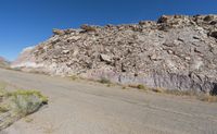 a desert like landscape with large rocks and green plants on the side of a dirt road