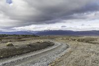 an empty road surrounded by barren mountains and bushes under a cloudy sky, as if in nature