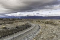 an empty road surrounded by barren mountains and bushes under a cloudy sky, as if in nature