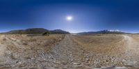 a very wide photo of a dirt road through a vast plain with a lone mountain in the distance