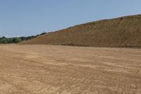 an empty field near a hill of dirt with some trees on one side and another in the distance