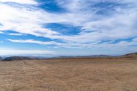 a man riding on top of a dirt hill under a blue sky filled with clouds