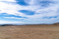 a man riding on top of a dirt hill under a blue sky filled with clouds