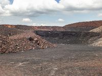 a pile of gravel sits next to some large rocks and gravel hills as the sky looks on