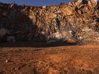 a man walking in front of a rocky cliff side with his backpack on the ground