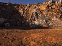 a man walking in front of a rocky cliff side with his backpack on the ground