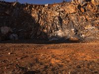 a man walking in front of a rocky cliff side with his backpack on the ground