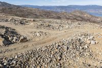 the dirt trail on the mountain is going down to the sea and mountains in the background