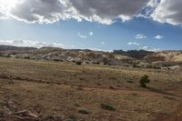 dirt trail through the desert with clouds above it and trees near an open grassy field