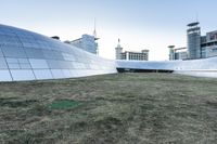 the outside of the building is designed to look like an oculus of architecture with curved metal walls, grass and lawn