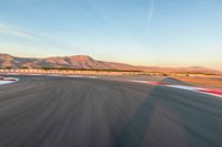 a photo of a dirt race track with sun setting in the distance of the track