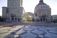 a view of several buildings and a square area with checkerboard flooring, with a large curved archway that stretches from the building to the front of several sides of the building