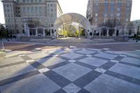 a view of several buildings and a square area with checkerboard flooring, with a large curved archway that stretches from the building to the front of several sides of the building