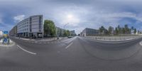 an empty street with the sun shining and several buildings in the background as seen through fisheye lens