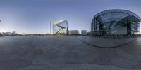 the circular panoramic photo shows a building surrounded by a large glass structure and several people walking around it