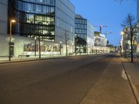 a paved street in the middle of buildings with tall windows at night, with car lights on