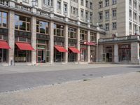 two people sit on a bench in front of a building with many windows and a red awning