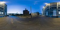 fisheye lens view showing an empty street and two large buildings at night with no traffic