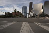 an empty city street in front of some very large buildings as the sun begins to set